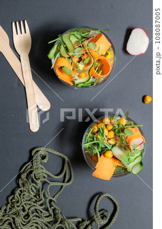 Two bowls with fresh vegetables, chickpeas and microgreens, on a black background, top view 108087005