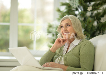 Senior woman sitting in sofa with laptop computer Senior woman sitting in sofa with laptop computer 108087401
