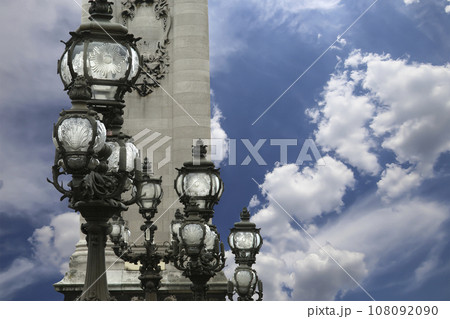 Lamp posts on Alexander III Bridge against the background of a beautiful sky with clouds. Paris, France. This arch bridge is one of the most beautiful river crossings in the world Lamp posts on Alexander III Bridge against the background of a beautiful sky with clouds. Paris, France. This arch bridge is one of the most beautiful river crossings in the world 108092090