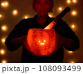Young woman holds a comically carved Halloween pumpkin with a cute face, illuminated by a burning 108093499