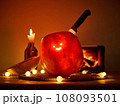 Halloween pumpkin with a comically carved face sits on a table, atmosphere is enhanced by warm 108093501