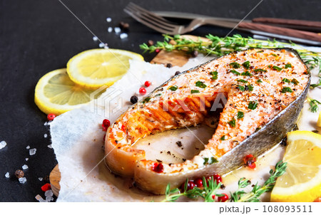 Fried salmon steak with thyme and lemon served on wooden plate on black table. Fried salmon steak with thyme and lemon served on wooden plate on black table. 108093511