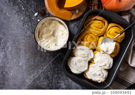 Freshly baked pumpkin cinnamon rolls or cinnabon with cream cheese on a dark stone background. Homemade seasonal autumn homemade pastry. View from above. Copy space. 108093691