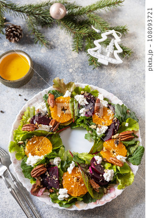 Christmas appetizer. Christmas wreath salad with beetroot, tangerines, feta cheese and pecans on the festive table. 108093721
