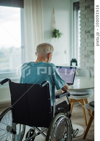 Senior man in a wheelchair write document on laptop. Elderly man using digital technologies, working on a notebook. Concept of seniors and digital skills. 108093916