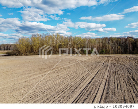 Arable field near the forest on a sunny day, aerial view. Agricultural field. 108094097