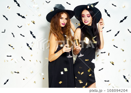 portrait of two happy young women in black witch halloween costumes. firecrackers in the background. 108094204
