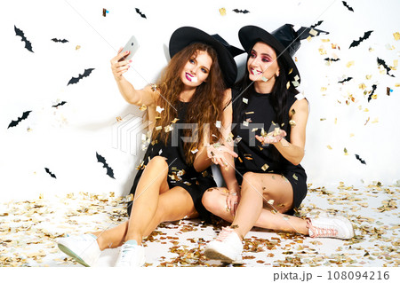 Portrait of two happy women in black witch halloween costumes on party over white background. Portrait of two happy women in black witch halloween costumes on party over white background. 108094216