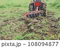Tractor Tilling the Soil with Vibrant Green Grass Background 108094877