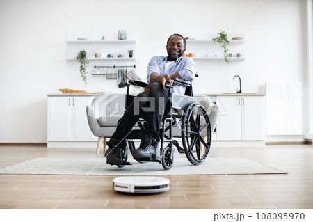 Smart robotic vacuum operated by happy african man with mobility impairment. 108095970