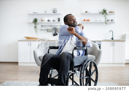 Joyous bearded man in wheelchair exercising stretching arms 108095977