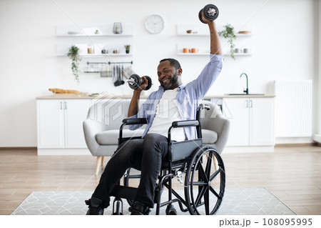 Man with limited mobility lifting weights at home workout Man with limited mobility lifting weights at home workout 108095995