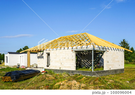 Unfinished residential house with white concrete block walls and a wooden beam truss roof structure Unfinished residential house with white concrete block walls and a wooden beam truss roof structure 108096004
