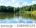 Pond with reflective water on a summer day, people swimming in the pond 108096324