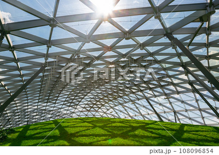 dome with glass roof under the open sky with sun glare, indoor safety park with green hill lit by sunlight green lawn, nobody. 108096854