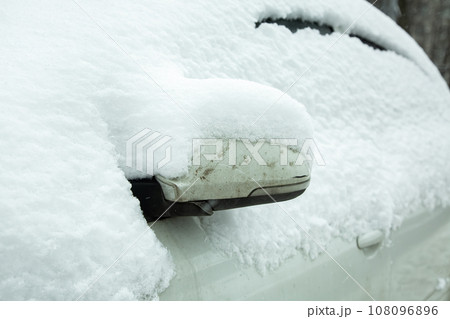 folded rearview mirror with a turn signal, white car covered with snow on a cold winter day, close-up details of a vehicle blocked by precipitation, nobody. 108096896