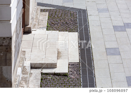corner of a building with stools at the entrance to an old crumbling building next to a stone sidewalk in sunny weather, close-up of architecture. 108096897