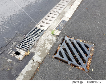 drainage system of an asphalt road from a sidewalk with a concrete curb dirty after rain, square iron and rectangular concrete gratings for rainwater drainage, nobody. drainage system of an asphalt road from a sidewalk with a concrete curb dirty after rain, square iron and rectangular concrete gratings for rainwater drainage, nobody. 108096976