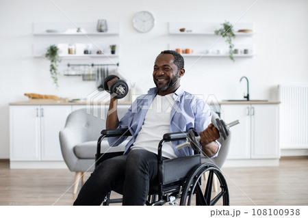 Person with disability raising dumbbells in kitchen interior Person with disability raising dumbbells in kitchen interior 108100938