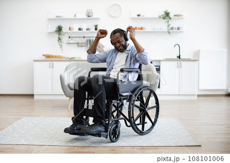 Man in wheelchair and headphones moving hands in air at kitchen table 108101006