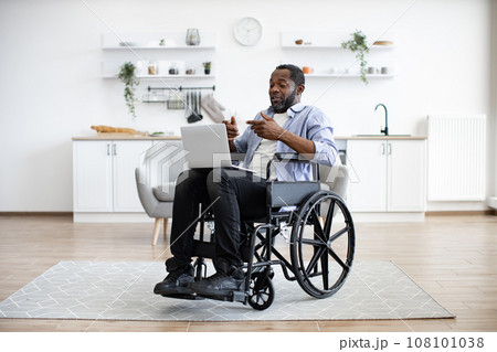 Man in wheelchair having video call on computer in apartment 108101038