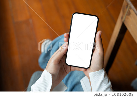 Top view of a woman using her smartphone while sitting indoors. A white-screen smartphone mockup. 108102608