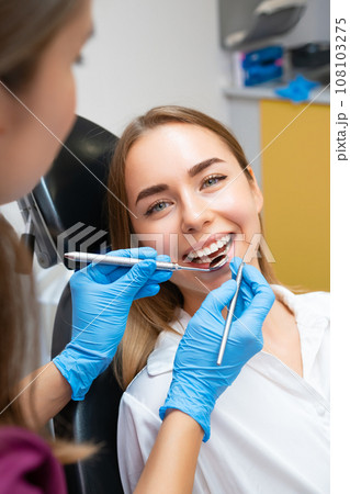 The dentist is performing dental treatment on a female patient with a flawless smile 108103275