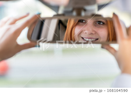 Young woman driver checking rear view mirror looking backwards while driving a car. 108104590