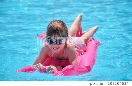 Young child girl relaxing on summer sun swimming on inflatable air mattress in swimming pool during tropical vacations. Summertime activities concept Young child girl relaxing on summer sun swimming on inflatable air mattress in swimming pool during tropical vacations. Summertime activities concept 108104684