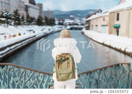 Woman tourist Visiting in Otaru, happy Traveler in Sweater sightseeing Otaru canal with Snow in winter season. landmark and popular for attractions in Hokkaido, Japan. Travel and Vacation concept 108105072
