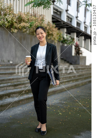 A confident and attractive millennial Asian businesswoman is standing outside of the building. A confident and attractive millennial Asian businesswoman is standing outside of the building. 108110437
