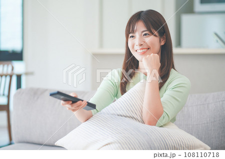 リビングのソファに座ってテレビのリモコンを操作する女性 108110718
