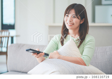 リビングのソファに座ってテレビのリモコンを操作する女性 108110719