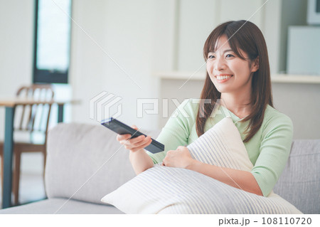 リビングのソファに座ってテレビのリモコンを操作する女性 108110720