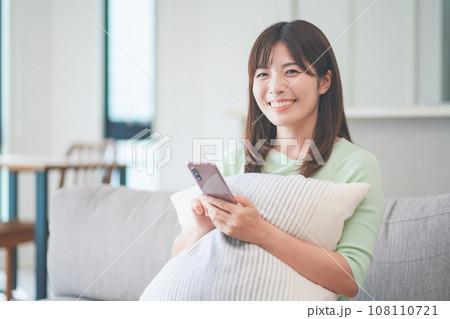リビングのソファに座ってスマートフォンを操作しながらくつろぐ女性 108110721