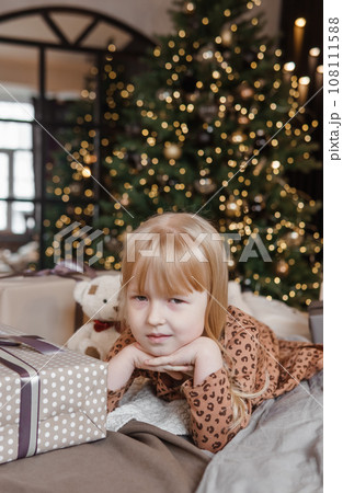 A little blonde girl is lying on a soft bed in a festive interior decorated in a New Year's style. The child is waiting for a New Year's gift. A little blonde girl is lying on a soft bed in a festive interior decorated in a New Year's style. The child is waiting for a New Year's gift. 108111588