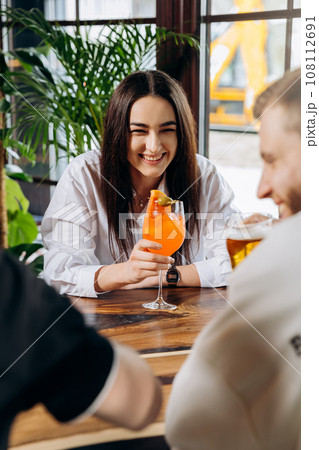 Smiling woman enjoying coctail in restaurant during rest with friends. Celebration and party concept Smiling woman enjoying coctail in restaurant during rest with friends. Celebration and party concept 108112691