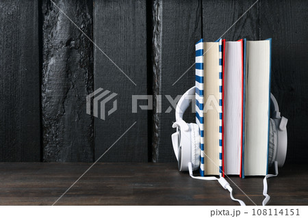 Headphones on books on dark wooden background, space for text Headphones on books on dark wooden background, space for text 108114151