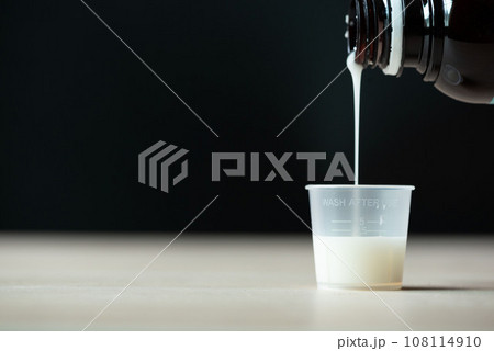 Pouring liquid white medication into plastic cup 108114910