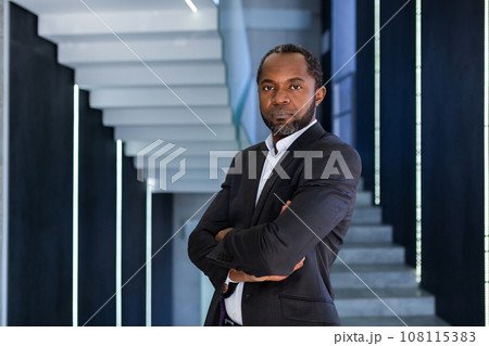 Portrait of serious confident businessman inside office with arms crossed, african american man looking concentrated and pensive at camera. Portrait of serious confident businessman inside office with arms crossed, african american man looking concentrated and pensive at camera. 108115383