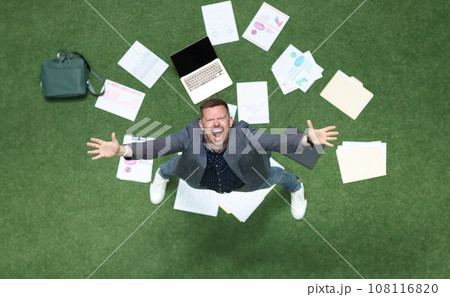 Man in suit throwing papers on green grass and yelling with his hands up top view 108116820