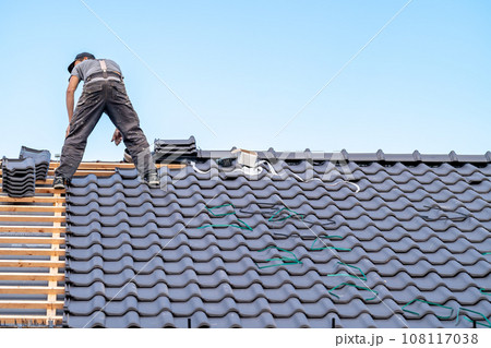 a craftsman on the roof of a bungalow installs a new roof ceramic covering 108117038
