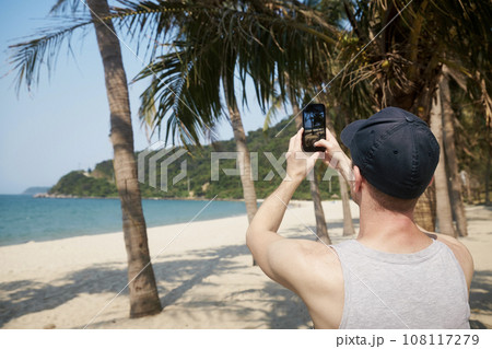 Man photographing with smart phone on idyllic sand beach. Man photographing with smart phone on idyllic sand beach. 108117279