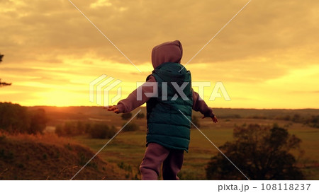 Little child spreads arms and waves hands playing airplane in wild park at sunset Little child spreads arms and waves hands playing airplane in wild park at sunset 108118237