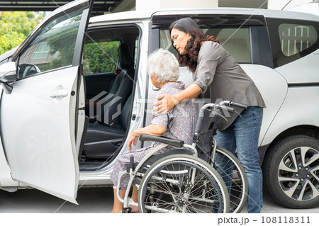 Caregiver help and support asian elderly woman sitting on wheelchair prepare get to her car to travel in holiday. 108118311