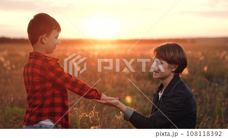 Boy places hand in hand of mother trusting to guide on field at sunset 108118392