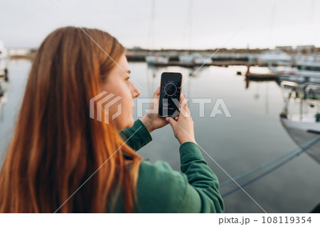 Concept a Hand Holding a Compass on smart phone. Young Woman Searching locations, walking along the waterfront, seaside. 108119354