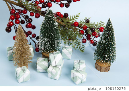 Composition with colorful gifts, a branch of holly with its red berries and christmas tree against a luminous sky-blue background. 108120276