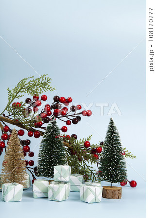 Composition with colorful gifts, a branch of holly with its red berries and christmas tree against a luminous sky-blue background. Composition with colorful gifts, a branch of holly with its red berries and christmas tree against a luminous sky-blue background. 108120277
