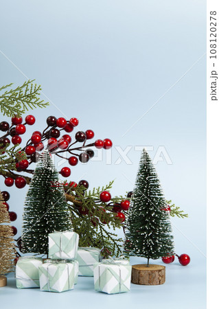 Composition with colorful gifts, a branch of holly with its red berries and christmas tree against a luminous sky-blue background. 108120278